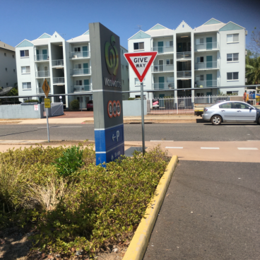 Sign for Woolworths, parking, and a GIVE WAY sign in front of apartment buildings on a sunny day.