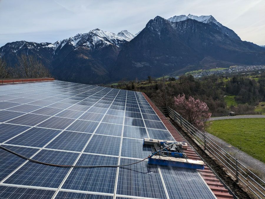 Solarpaneele auf einem Dach, im Hintergrund Berge und ein blühender Baum.