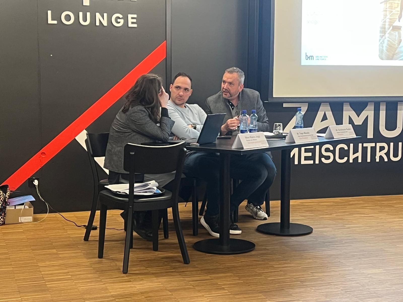 Trois personnes assises à une table basse lors d'une table ronde sur une scène de conférence