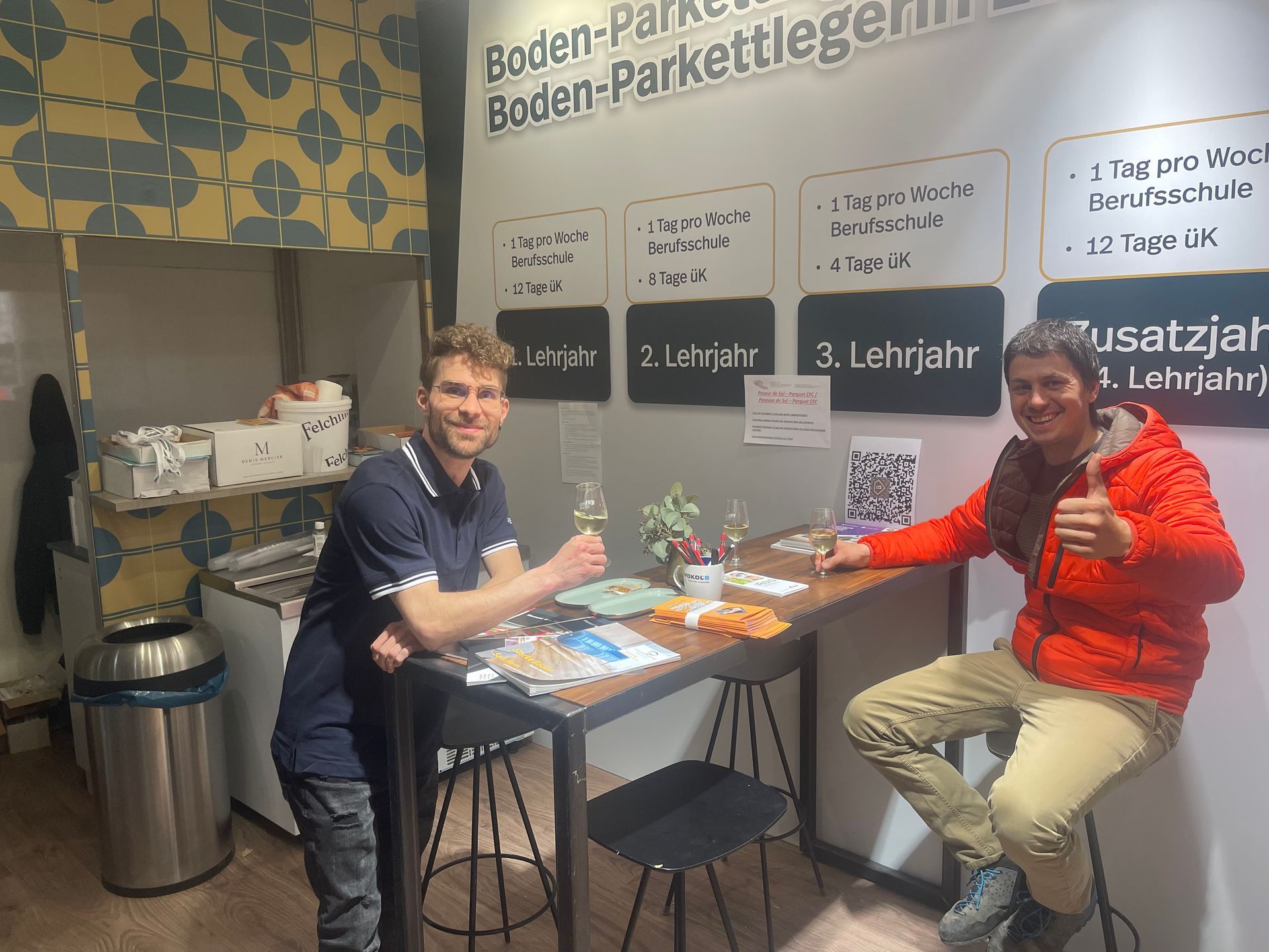 Zwei Männer sitzen an einem Tisch und zeigen ihre Daumen nach oben.