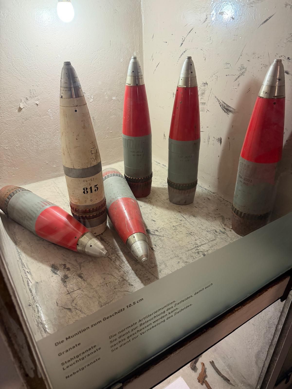 Six obus d'artillerie rouges et argentés sont exposés sur un piédestal de musée avec une plaque explicative.