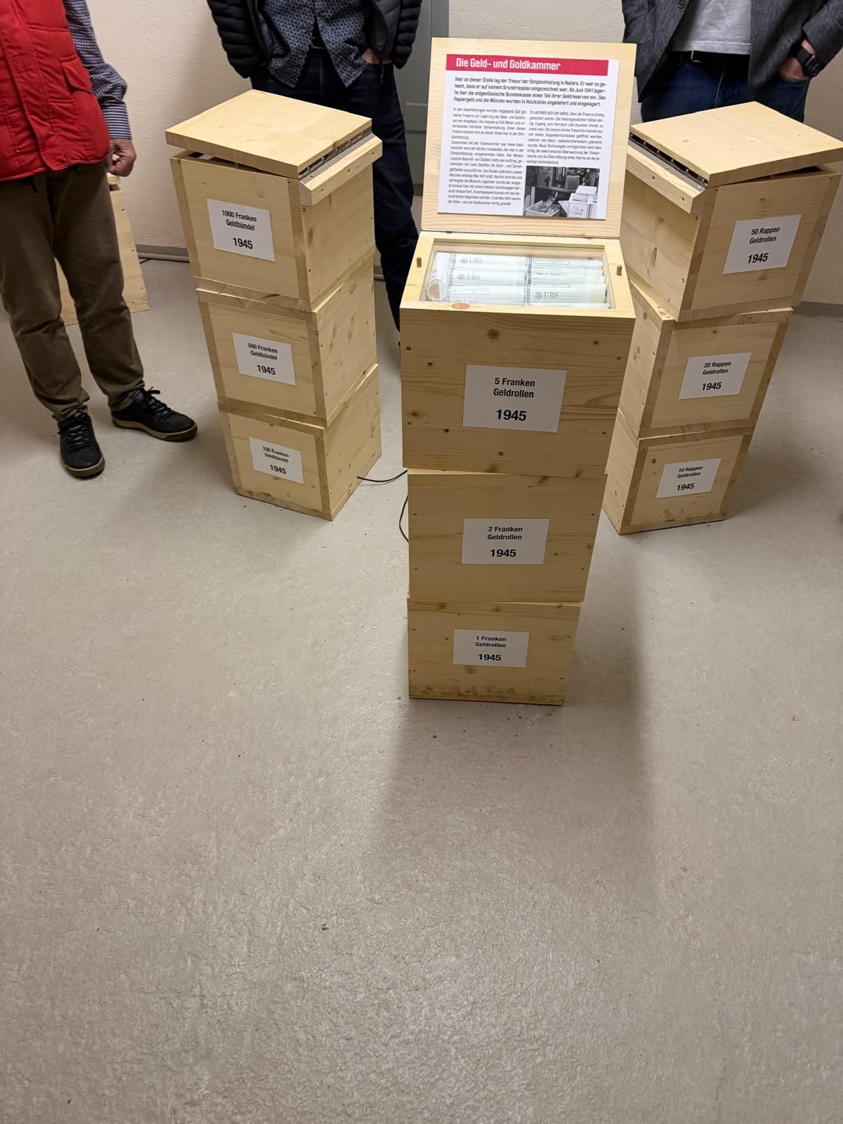 Des cartons empilés sur des tables à côté d'un panneau dans un couloir, des personnes se tenant à proximité.