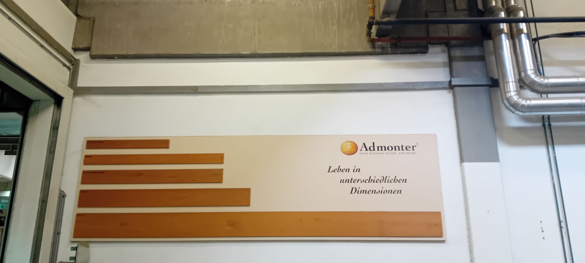 Panneau mural à rayures brunes et logo, fixé sur un mur blanc intérieur près des canalisations