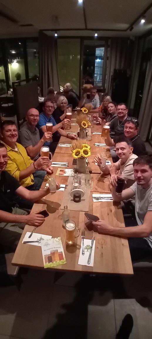 Des personnes assises autour d'une longue table à manger lèvent leurs verres dans un restaurant à l'éclairage chaleureux.