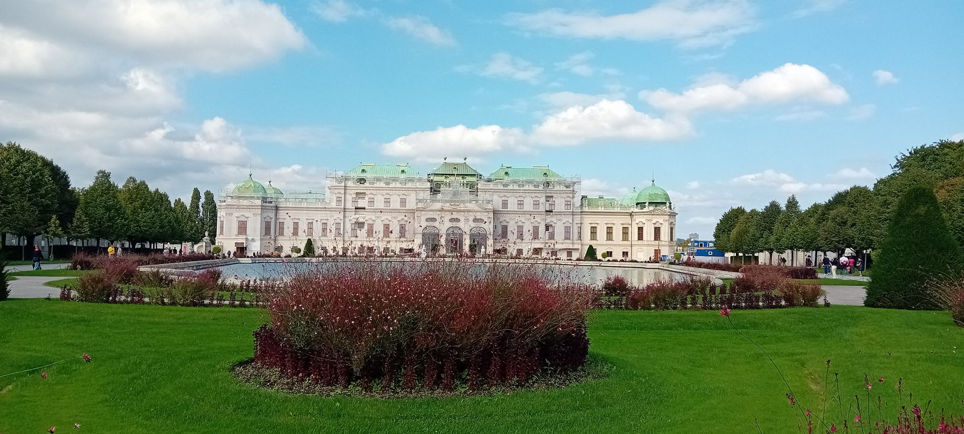 Grand palais avec une pelouse verte et des parterres de fleurs rouges sous un ciel partiellement nuageux