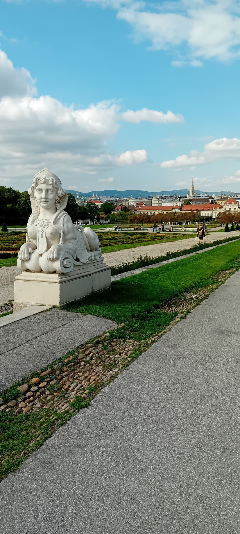 Statue de lion en pierre au bord d'un chemin pavé surplombant une ville et des bâtiments aux toits rouges sous un ciel bleu