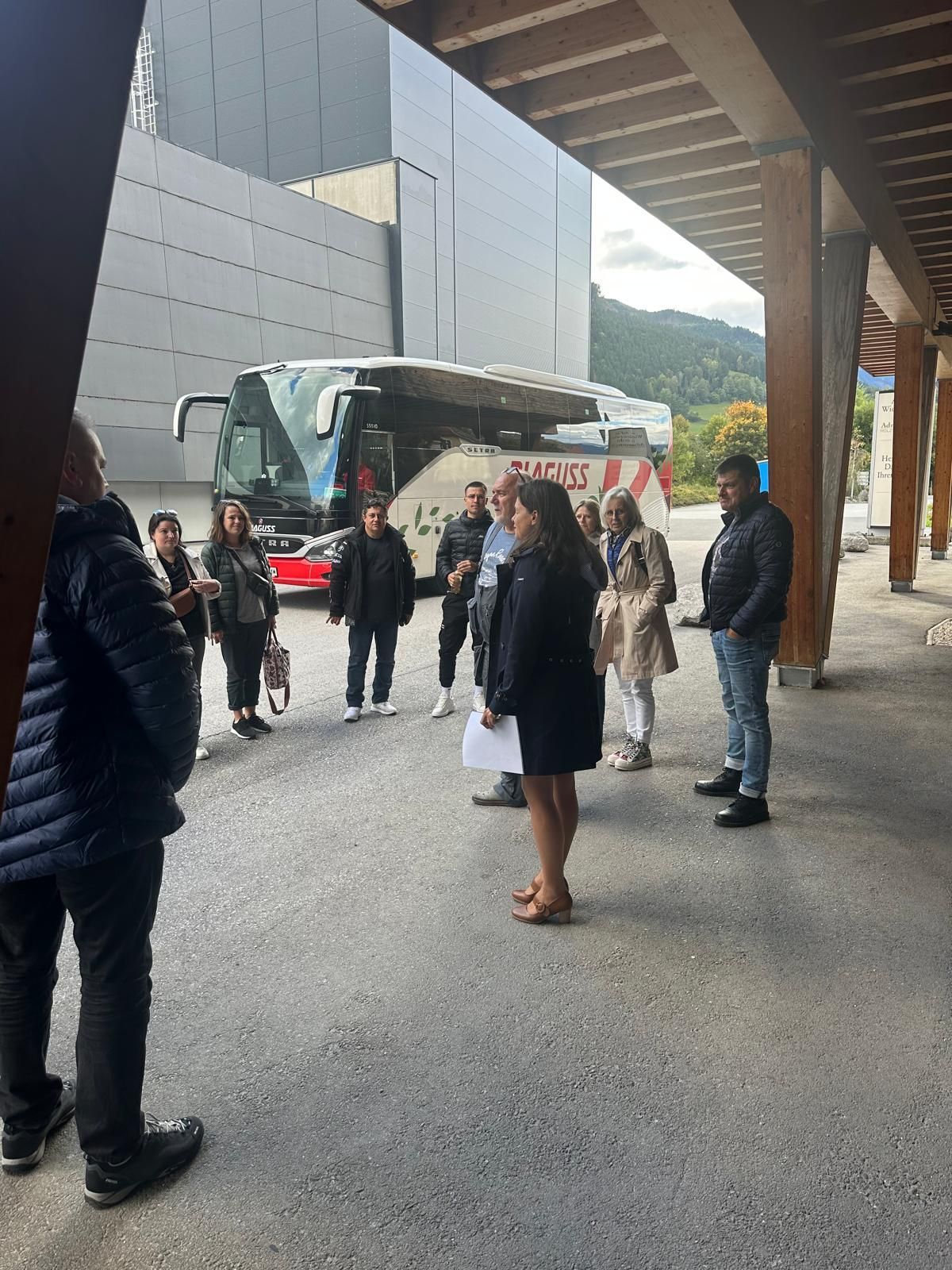 Des personnes se tiennent près d'un bus blanc sous un passage couvert, à proximité d'un bâtiment moderne.