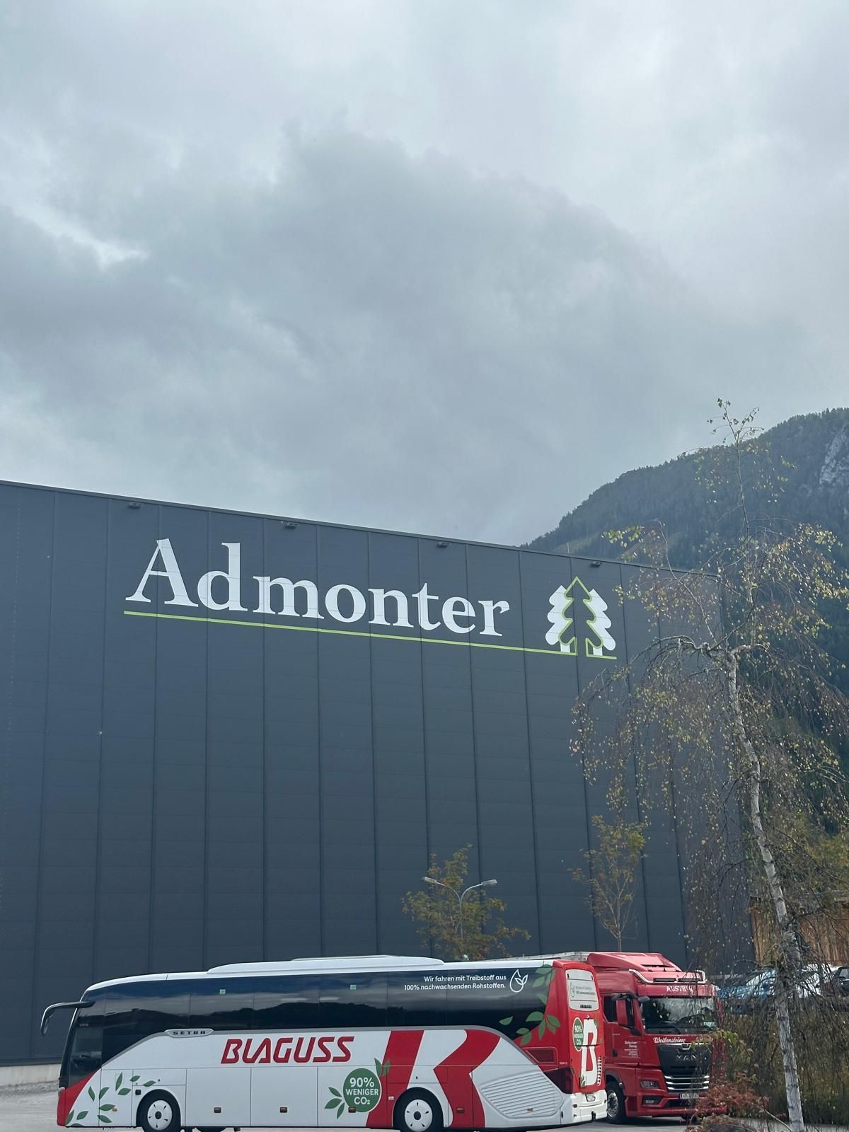 Bâtiment Admonter avec des montagnes nuageuses en arrière-plan et des bus BÜGUSS rouges et blancs garés devant