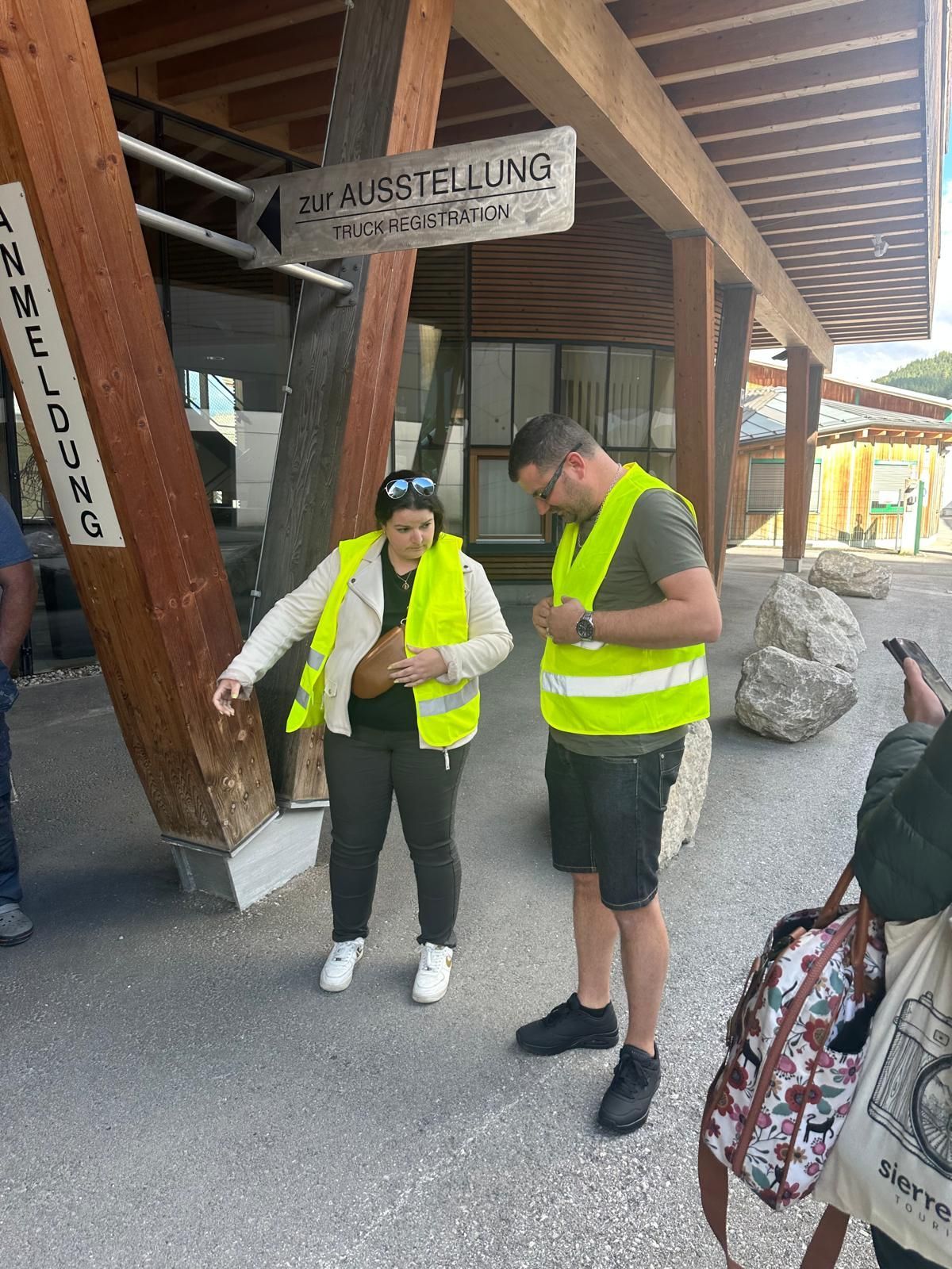 Deux personnes portant des gilets de sécurité fluo se tiennent sous un abri en bois, l'une d'elles pointant du doigt une carte en papier.