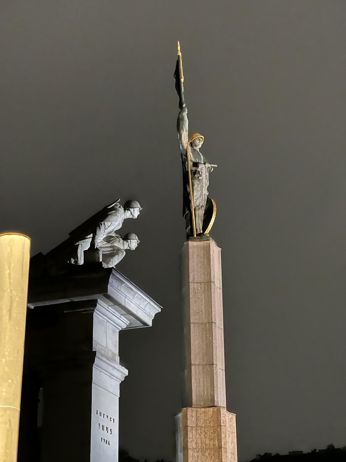 Vue nocturne d'un haut monument avec une figure sur un piédestal de pierre se détachant sur le ciel sombre