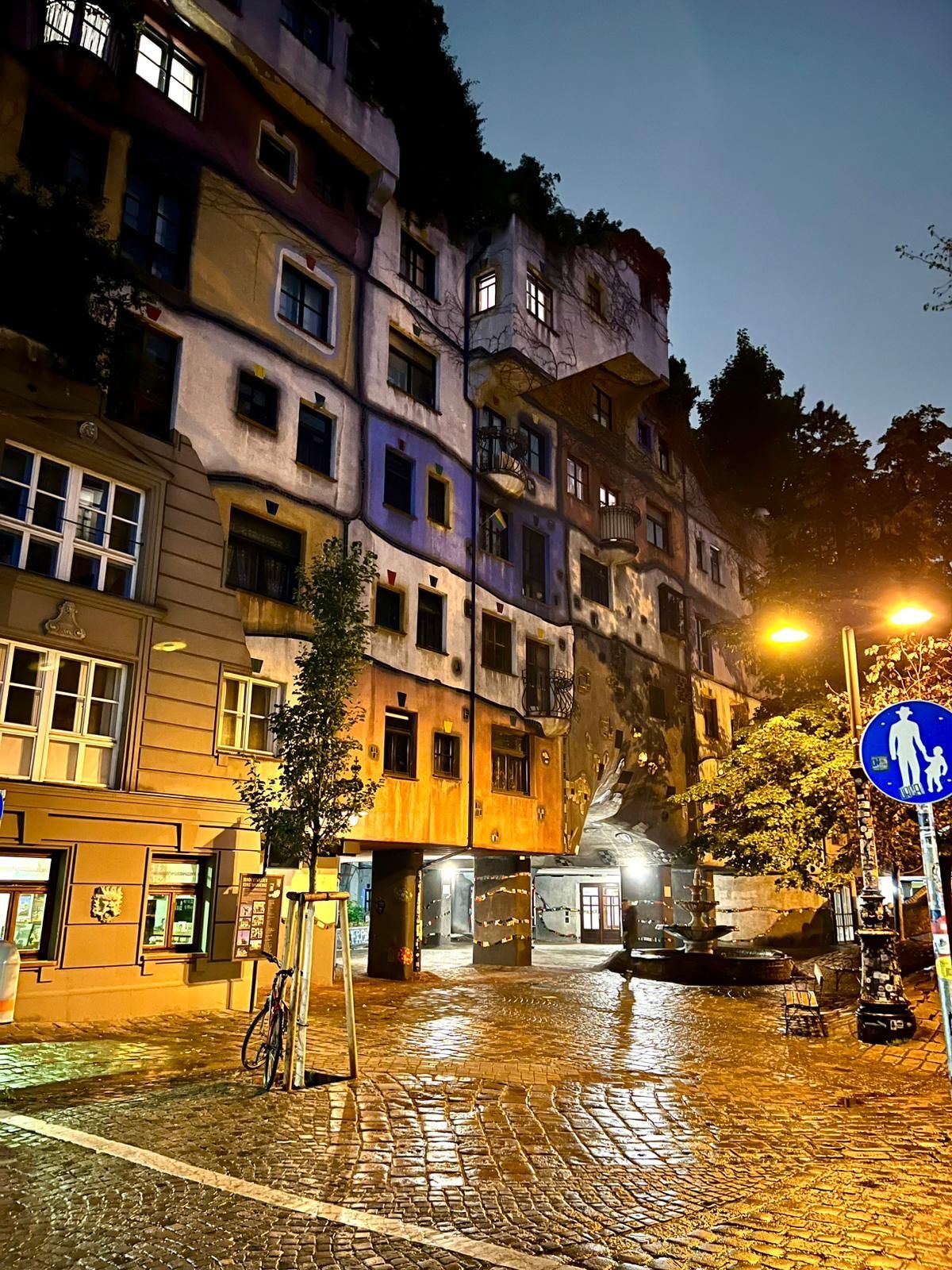 Rue pavée pluvieuse la nuit, avec des réverbères scintillants et de vieux bâtiments colorés à flanc de colline