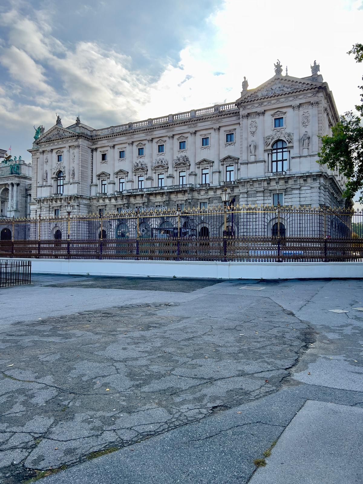 Palais historique orné derrière une clôture en fer forgé sous un ciel nuageux