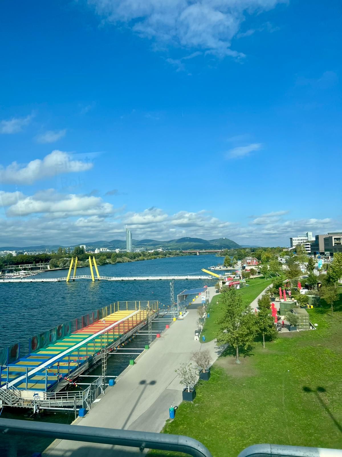 Promenade colorée au bord de l'eau avec une rivière, des bateaux amarrés, une pelouse verte et un ciel d'un bleu éclatant