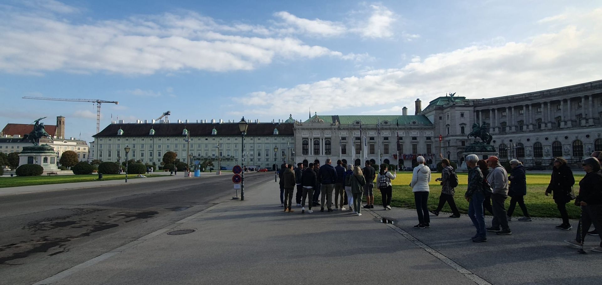 Des gens se promènent sur une grande place ouverte, à côté d'un bâtiment historique, sous un ciel dégagé.