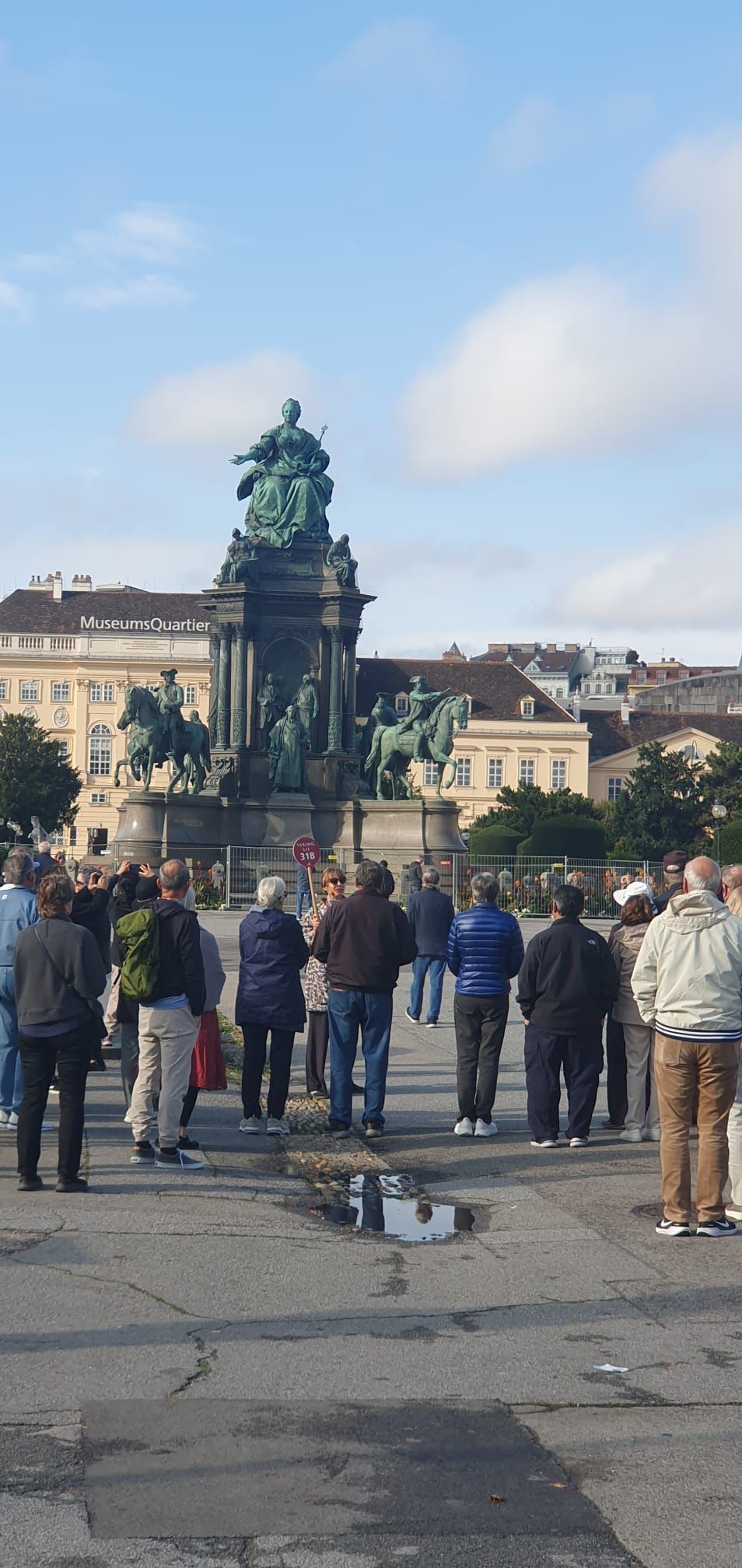 Une foule s'est rassemblée sur une place face à une statue verte ornée, sous un ciel nuageux.