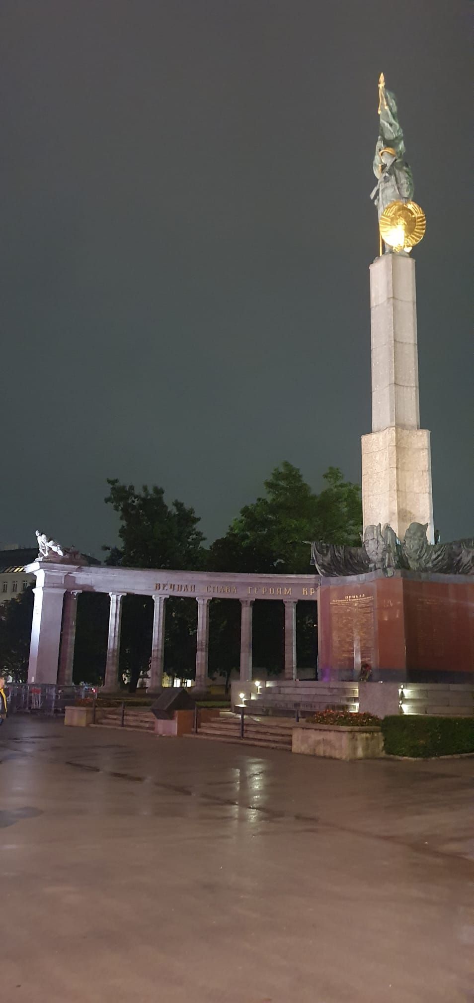 Monument nocturne surmonté d'un dôme doré illuminé, jouxtant un pavillon à colonnes et une place humide.