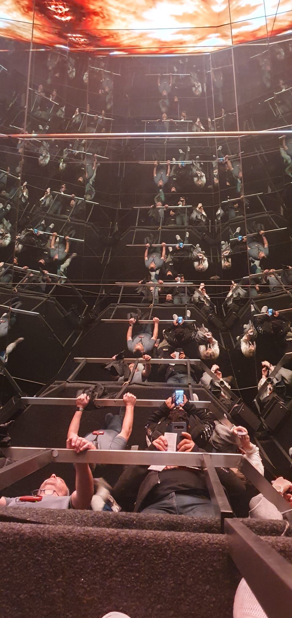 Des passagers dans une tour de chute intérieure plongée dans l'obscurité, les mains levées alors que le wagon plonge sous des lumières orange