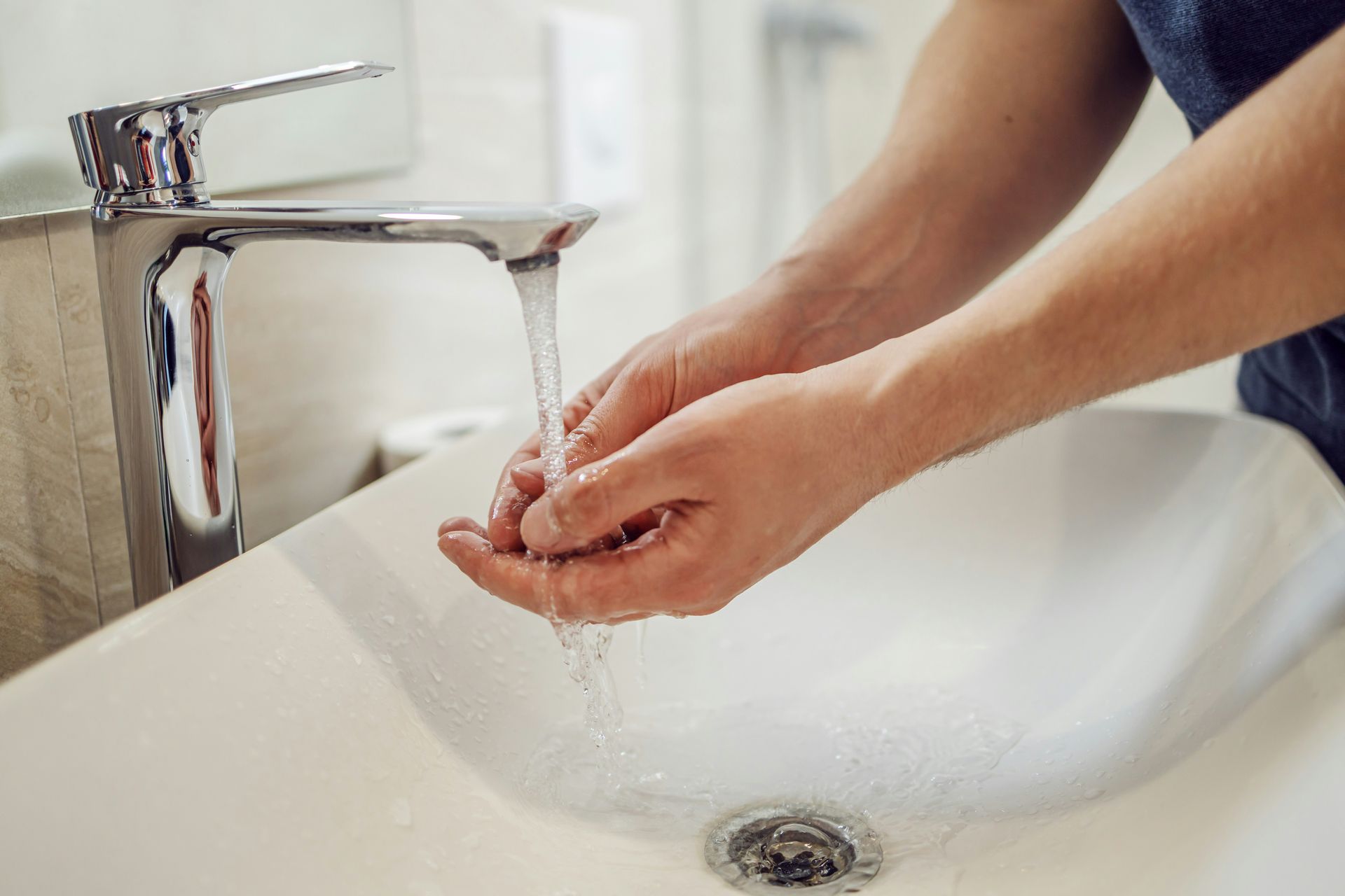 Hands washing under running water at a white sink with a chrome faucet