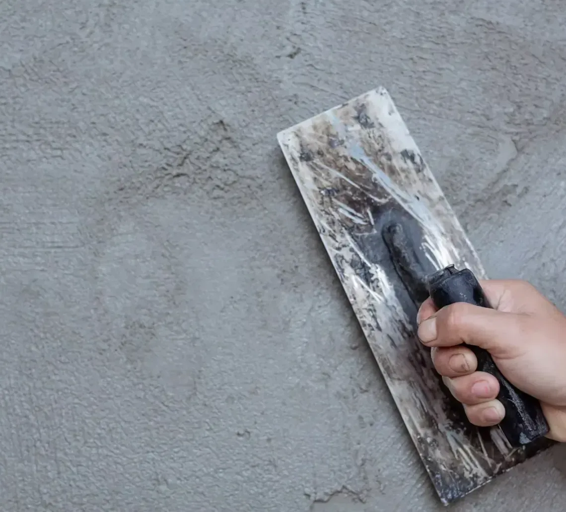 Hand smoothing gray plaster on a wall with a trowel