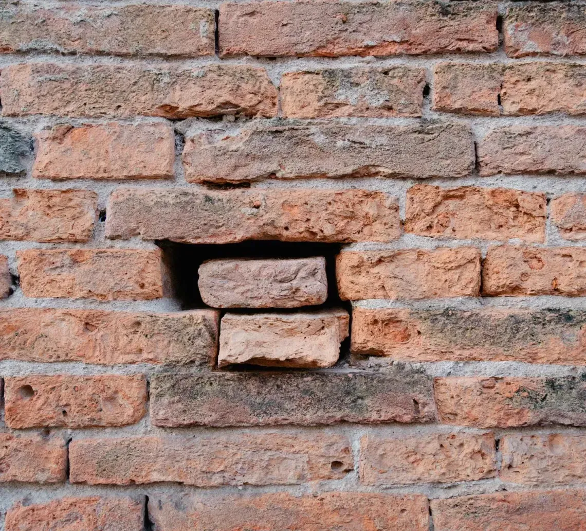 Old brick wall with a small rectangular hole exposing two bricks inside