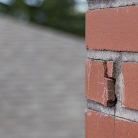 Damaged red brick corner with a chipped brick and cracked mortar on a building wall