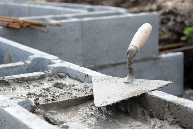 Worker smoothing wet concrete with a trowel on a masonry block wall