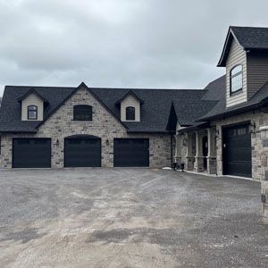 Large stone house with three garage doors and a wide gravel driveway under a cloudy sky