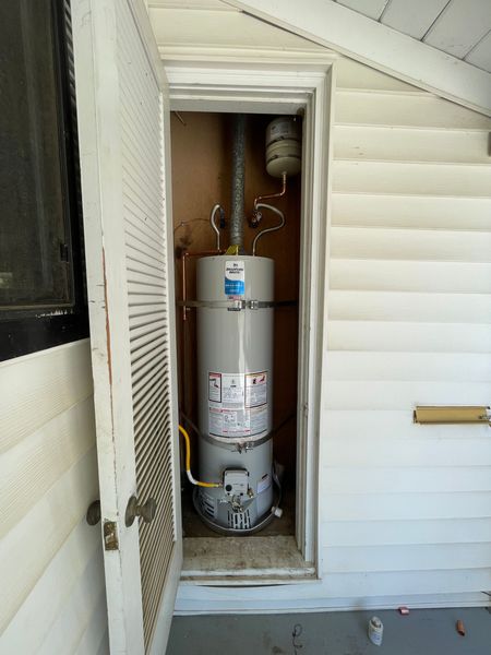 Water heater in a narrow outdoor utility closet beside a house exterior.