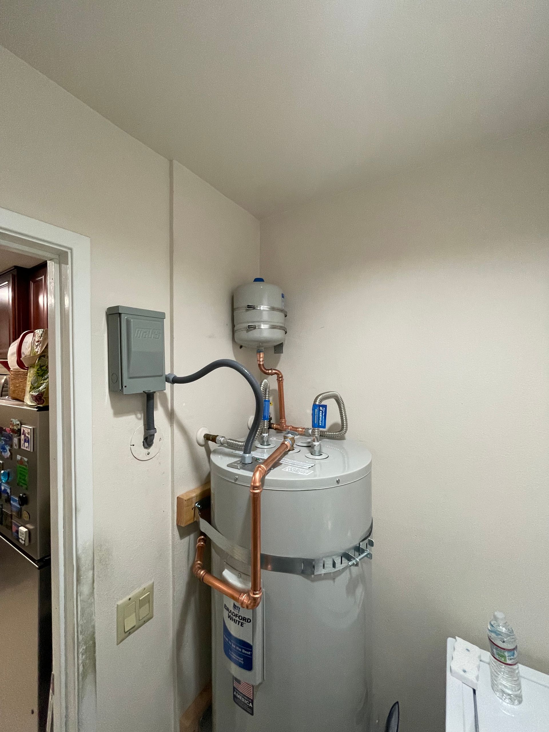 Utility closet with water heater, pipes, and an electrical panel mounted on the wall.