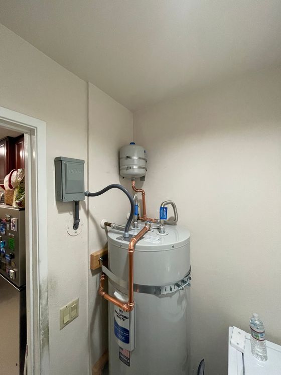 Utility closet with a water heater and pipes next to an electrical panel.