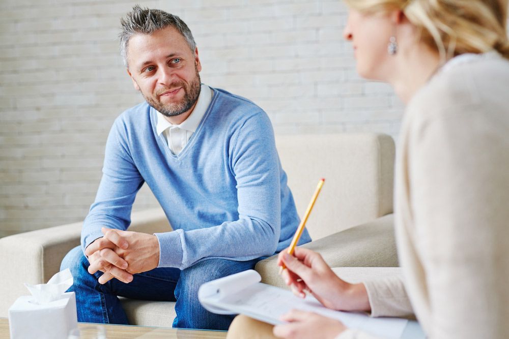 A Man is Sitting on a Couch Talking to a Woman — Living Well Psychology Clinic in Erina, NSW
