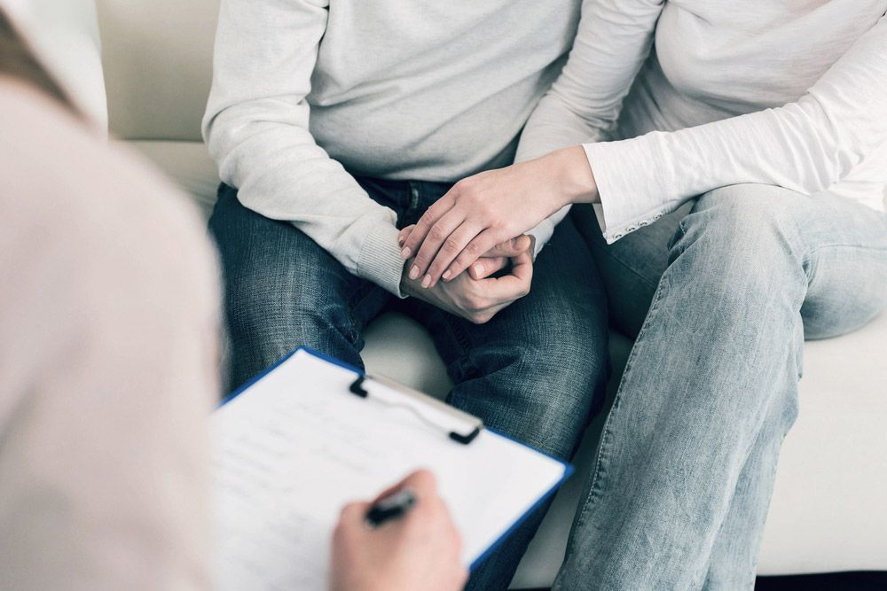 A Man and a Woman Are Holding Hands While Sitting on a Couch — Living Well Psychology Clinic in Erina, NSW