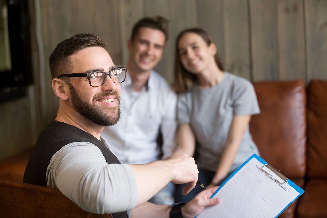 A Man is Holding a Clipboard in Front of a Couple Sitting on a Couch — Living Well Psychology Clinic in Erina, NSW