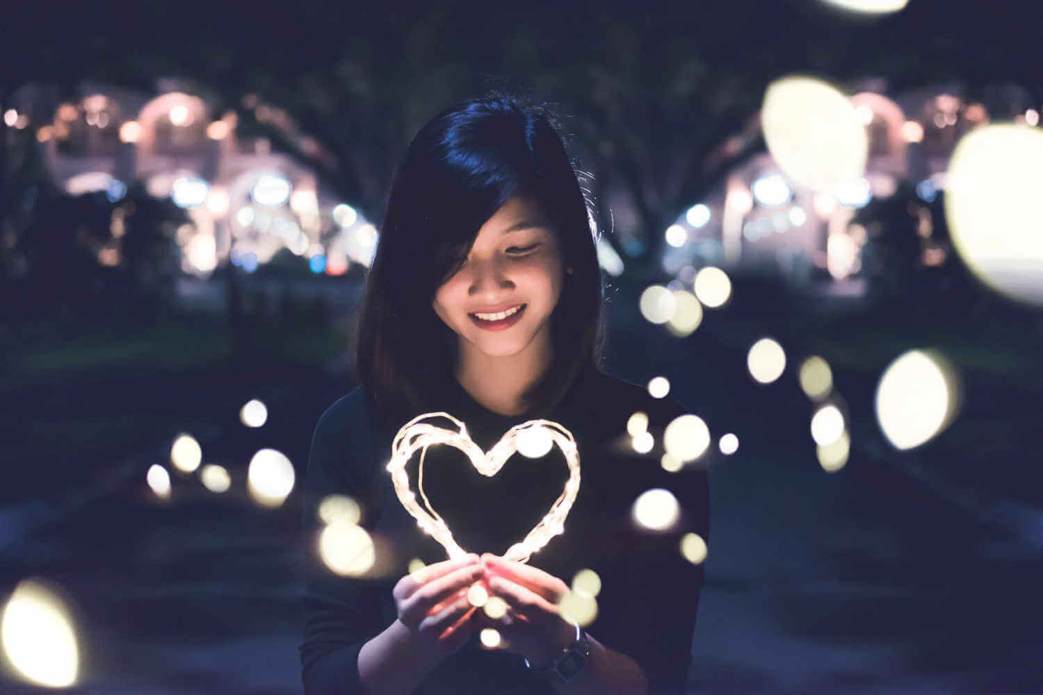A Woman is Holding a Heart Made of Lights in Her Hands — Living Well Psychology Clinic in Erina, NSW