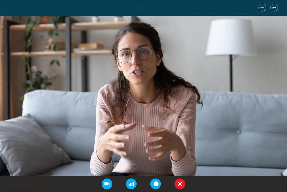 A Woman is Sitting on a Couch Talking on a Video Call — Living Well Psychology Clinic in Erina, NSW