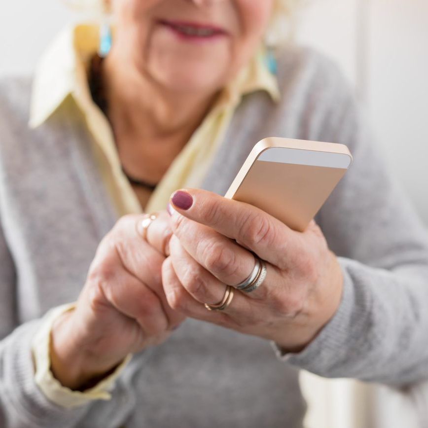 A person wearing a grey sweater and yellow collared shirt holding a smartphone with both hands.