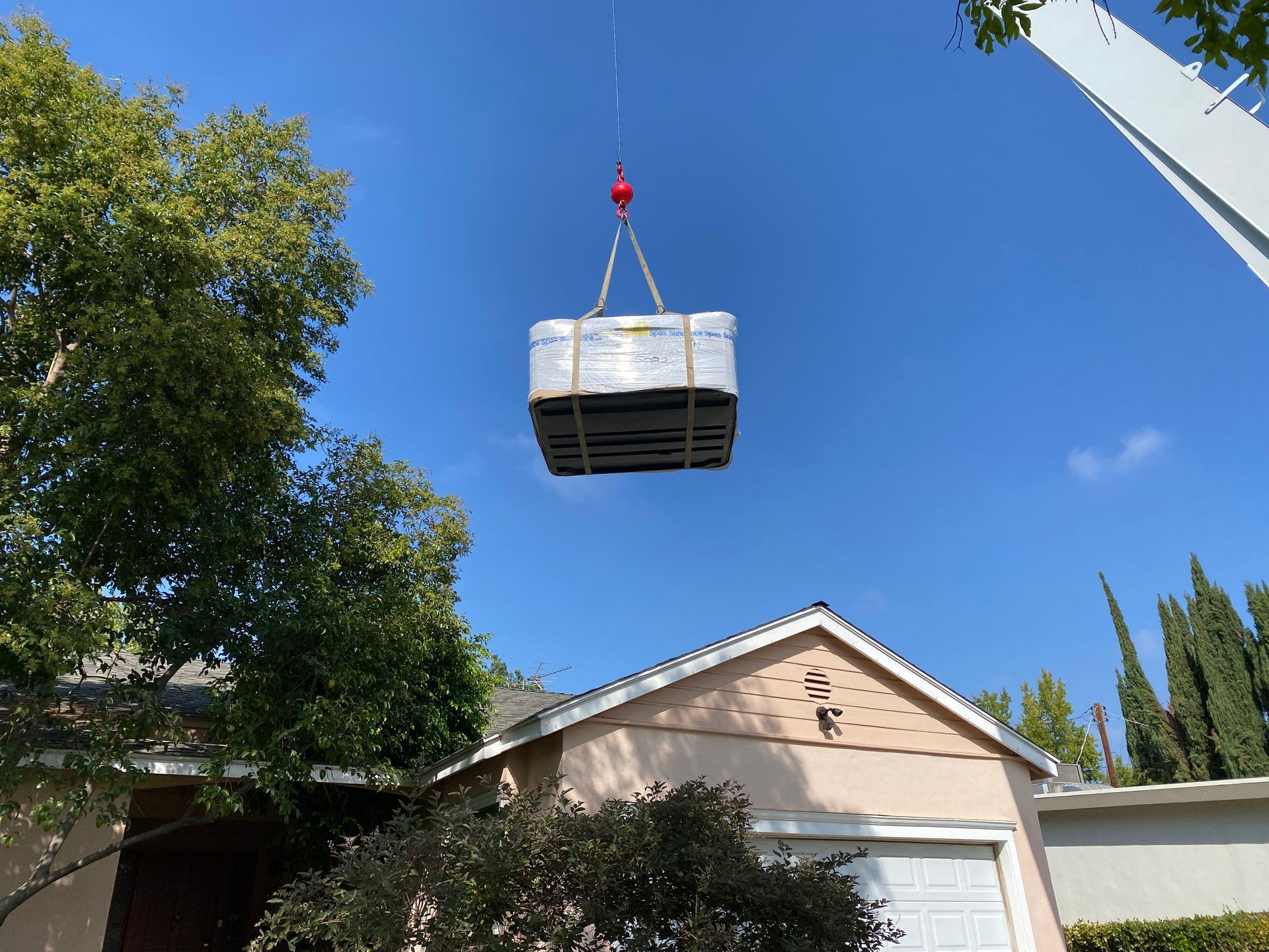 Large wooden hot tub being lifted by a red crane over an outdoor patio area.