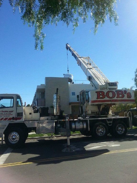 Tow truck with raised crane parked on a sunny street beside a building and tree branches