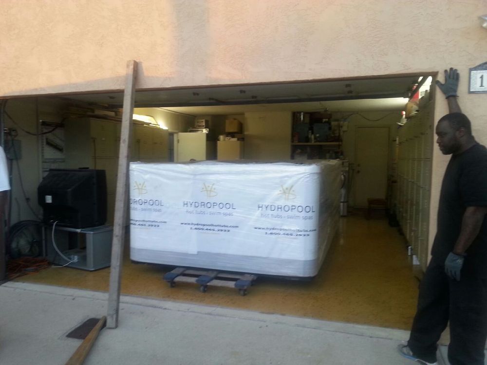 Open garage with a large boxed appliance on a pallet and a man standing at the right side