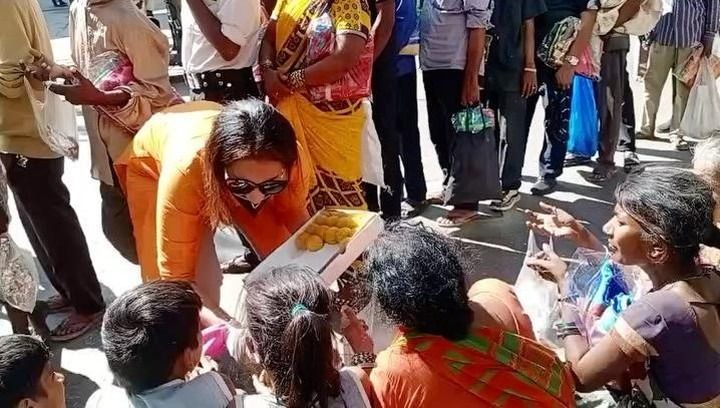 A woman is giving food to a group of people sitting on the ground.