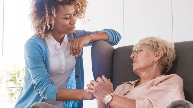 A woman is sitting on a couch holding the hand of an elderly woman.