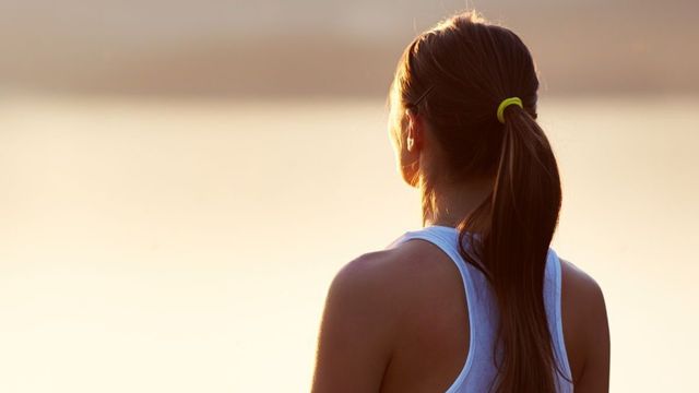 The woman is wearing a ponytail and looking at the water.