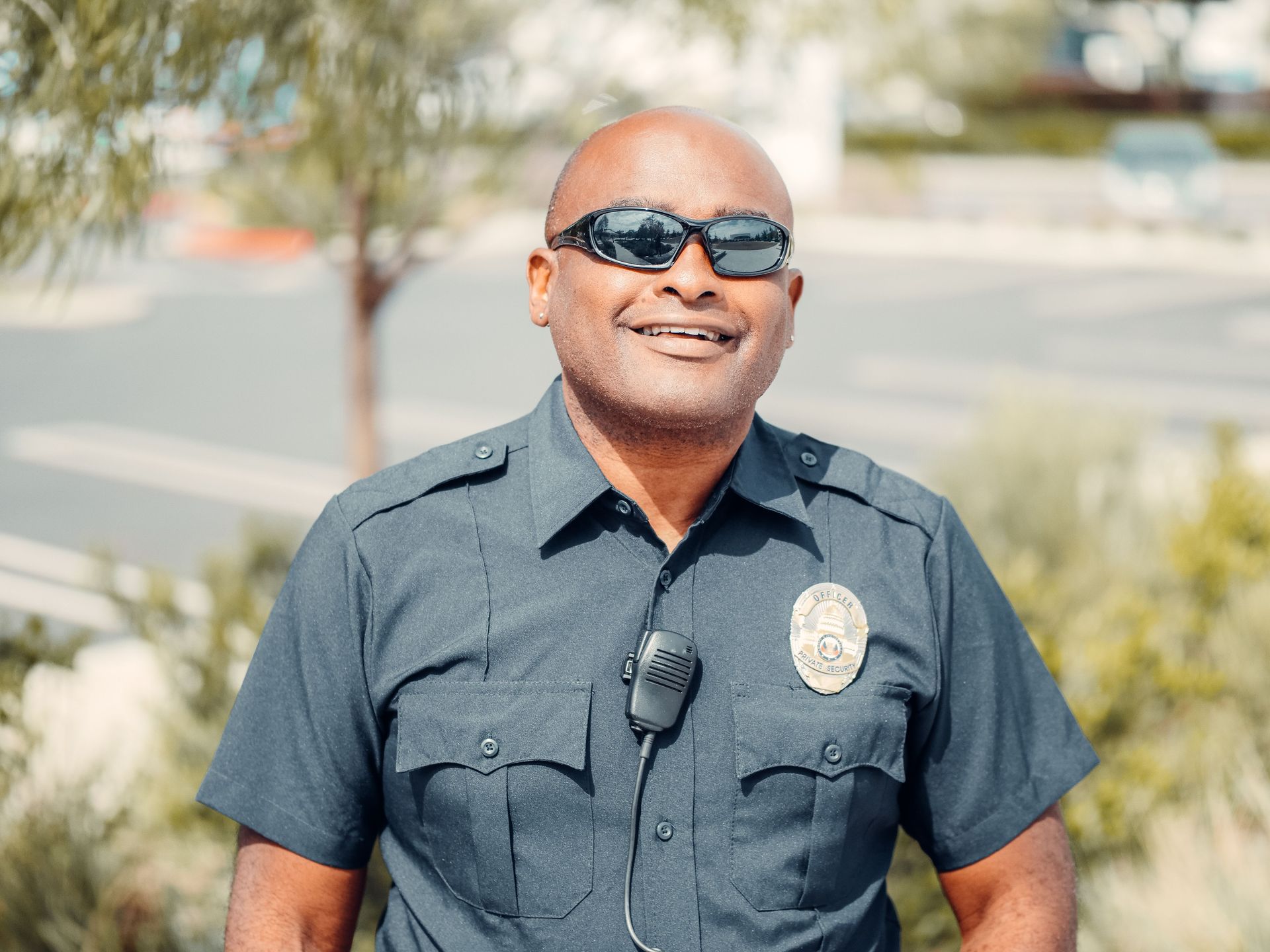 Smiling officer in dark uniform and sunglasses standing outdoors in bright sunlight