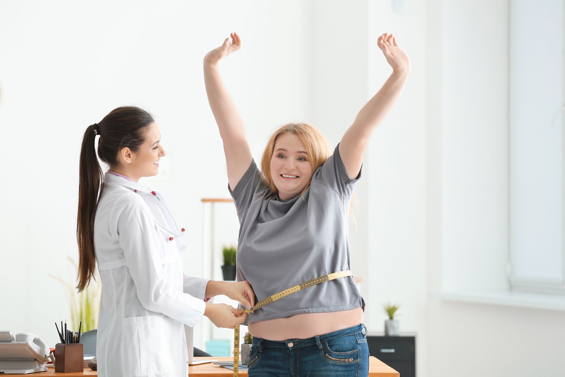 A doctor assists a woman in measuring her stomach, while the patient joyfully lifts her arms.
