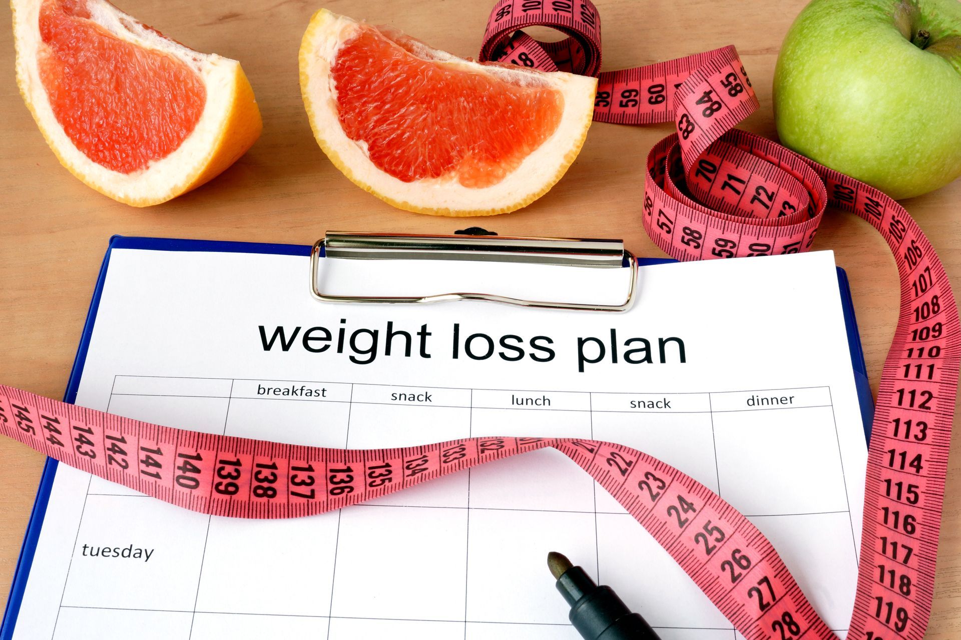 Weight loss plan chart with measuring tape, grapefruit, and green apple.