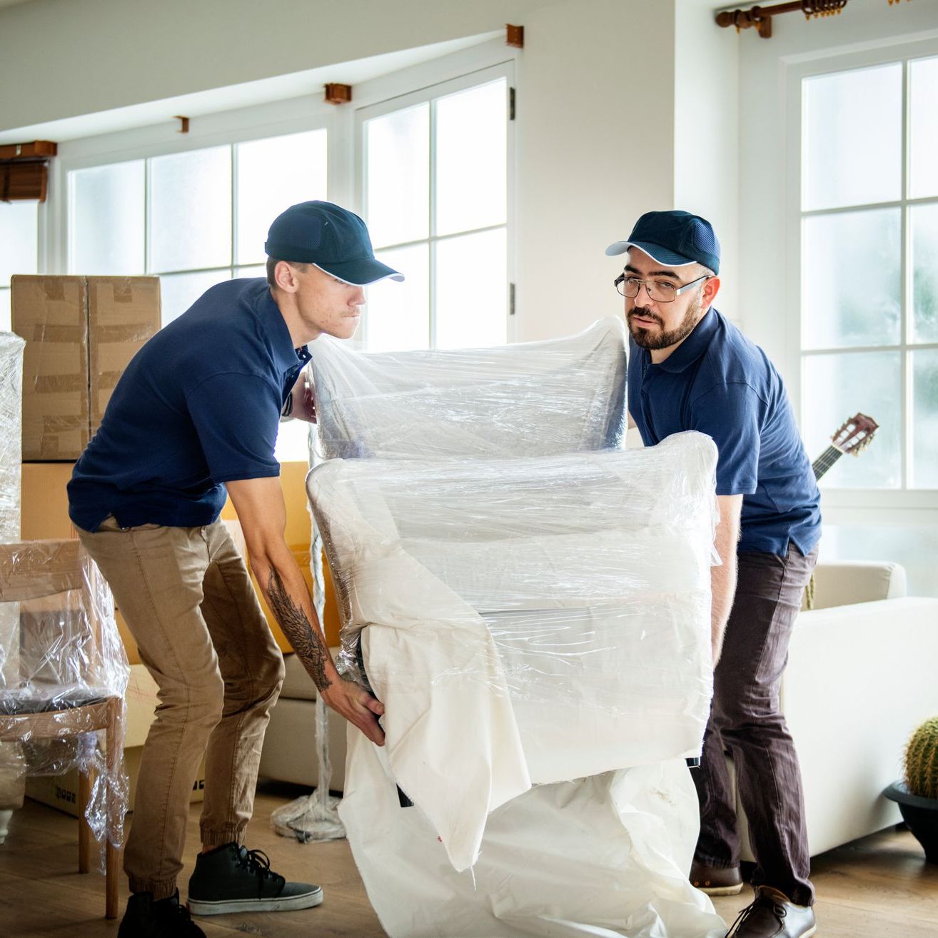 two men are carrying a large piece of furniture wrapped in plastic .