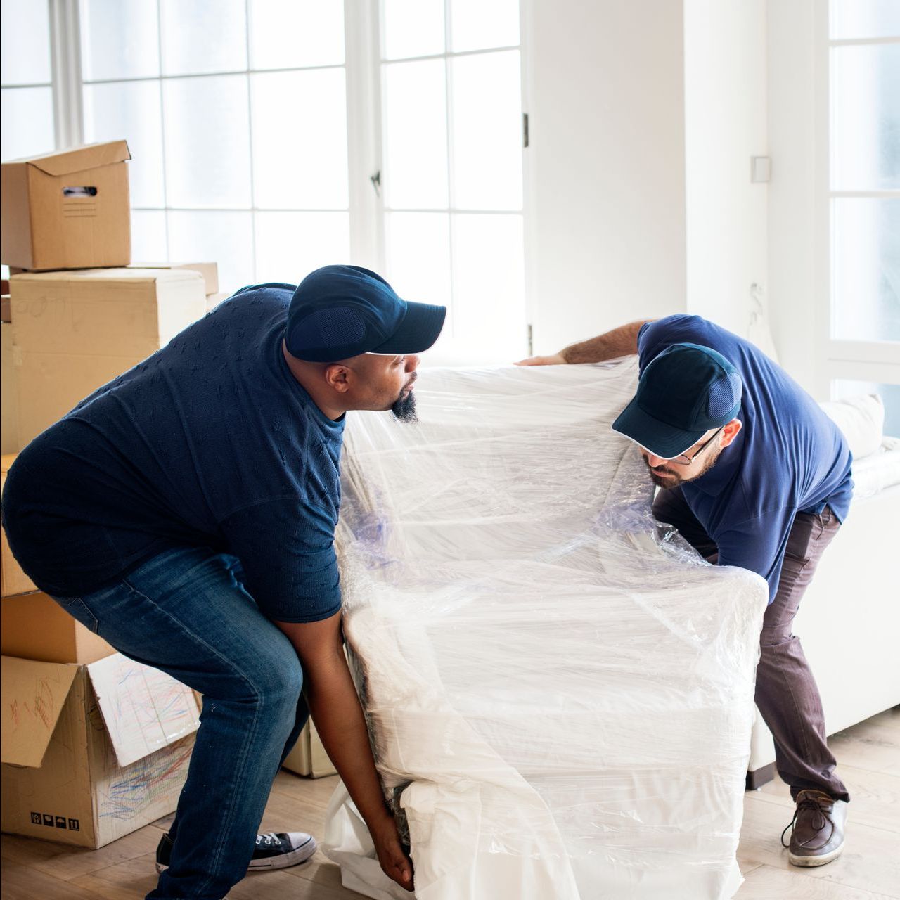 two men are wrapping a couch in plastic in a living room