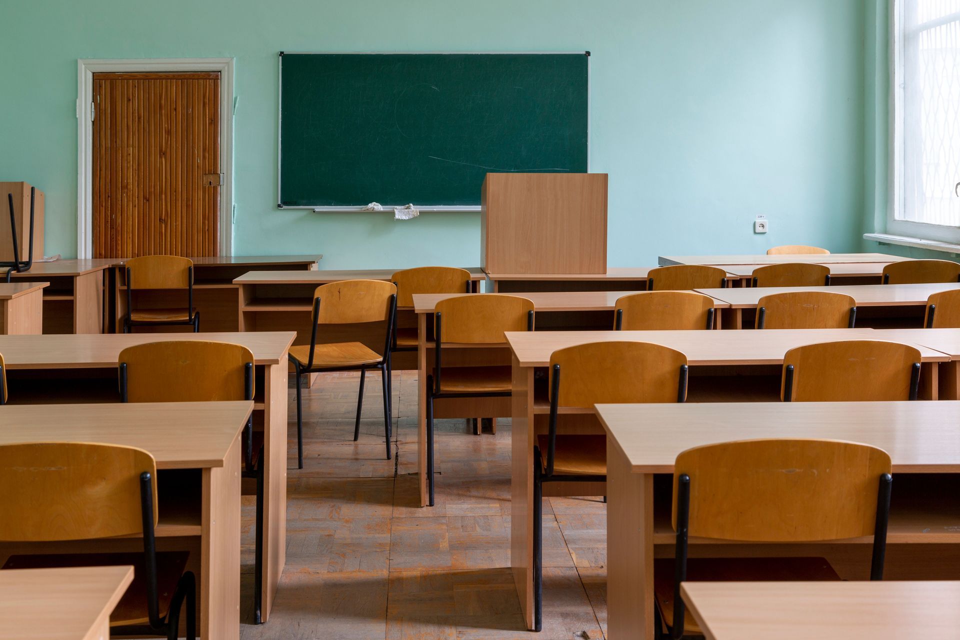 Empty classroom with wooden desks, green chalkboard, and large windows