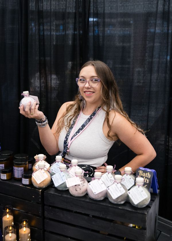 Vendor booth with black tablecloth, purple sign, and jewelry displays in a convention hall