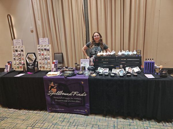 Vendor booth with black tablecloth, purple sign, and jewelry displays in a convention hall